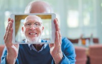 Portrait of happy senior man taking self portrait through digital tablet in nursing home